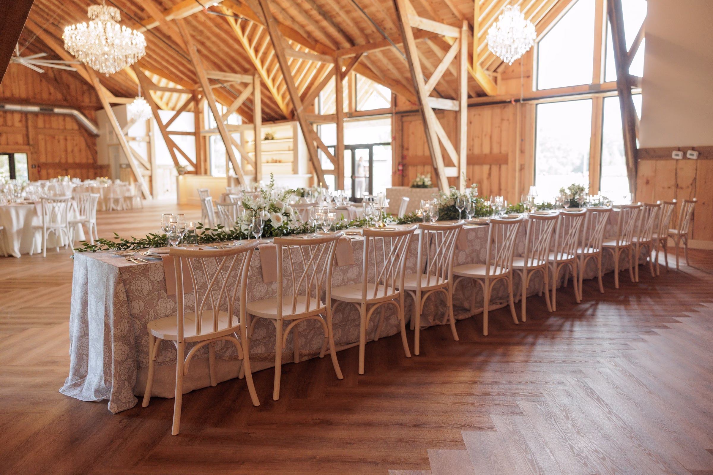 Elegantly decorated long head table with white floral garland centerpieces and crystal chandeliers in the rustic barn wedding venue The Grand in York SC near Charlotte NC