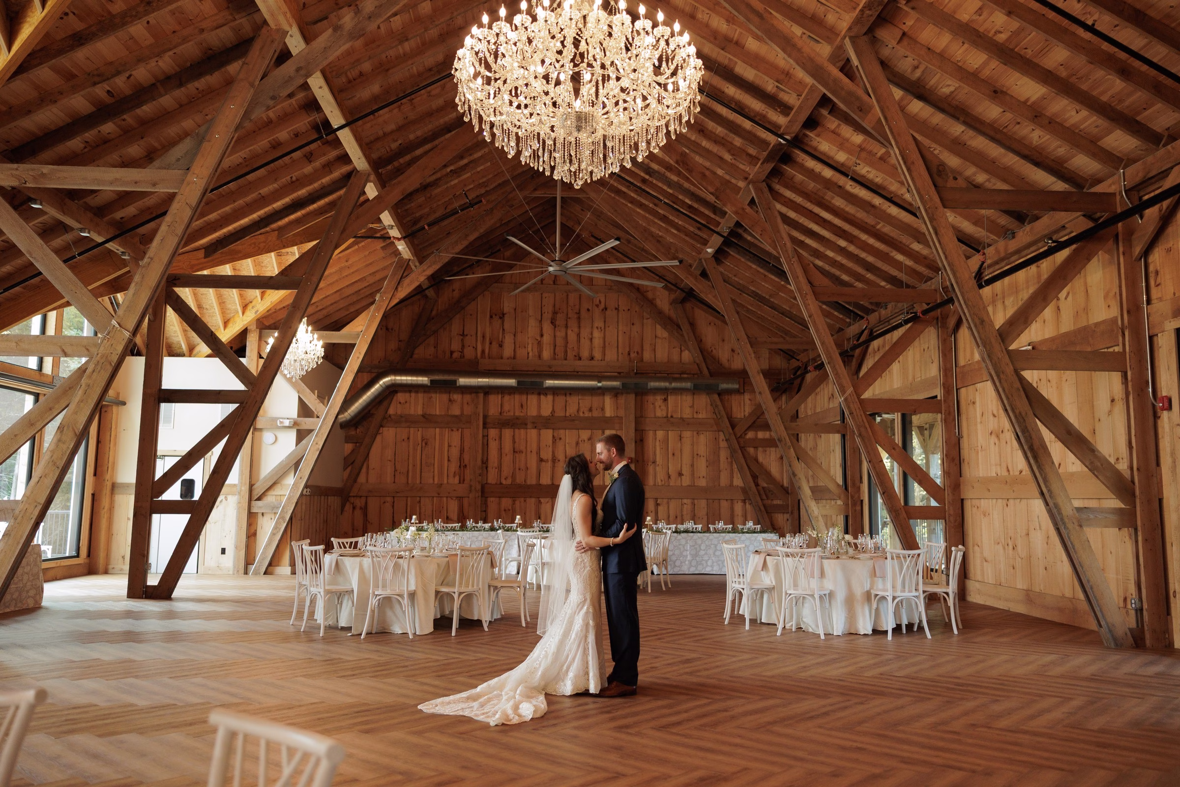 Bride and groom share an intimate moment on the herringbone dance floor of The Grand wedding venue in York SC, a rustic barn reception hall with soaring timber frame ceilings and crystal chandeliers near Charlotte NC