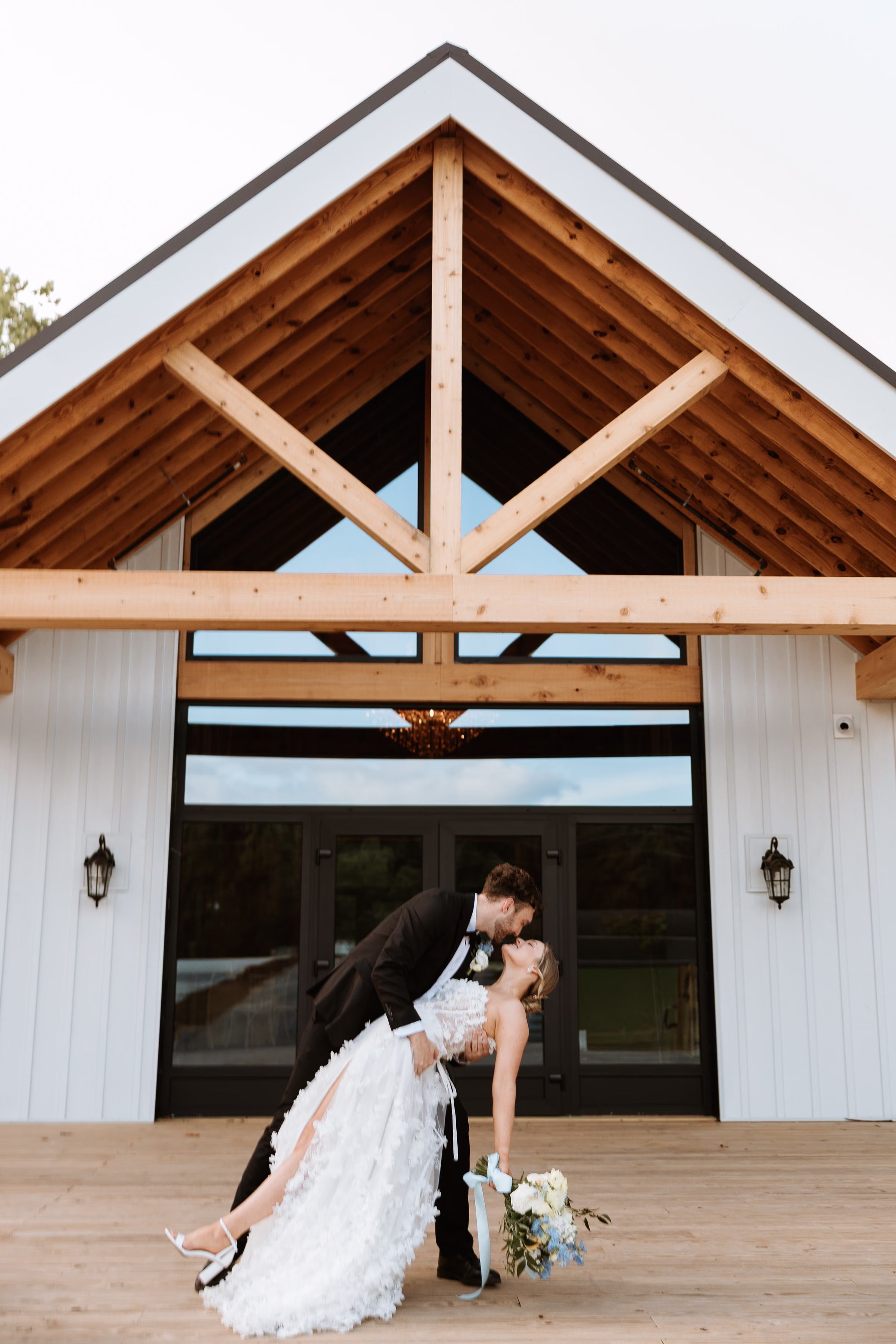 Bride and groom share a romantic dip kiss in front of the grand timber frame entrance at The Grand wedding venue in York SC near Charlotte NC