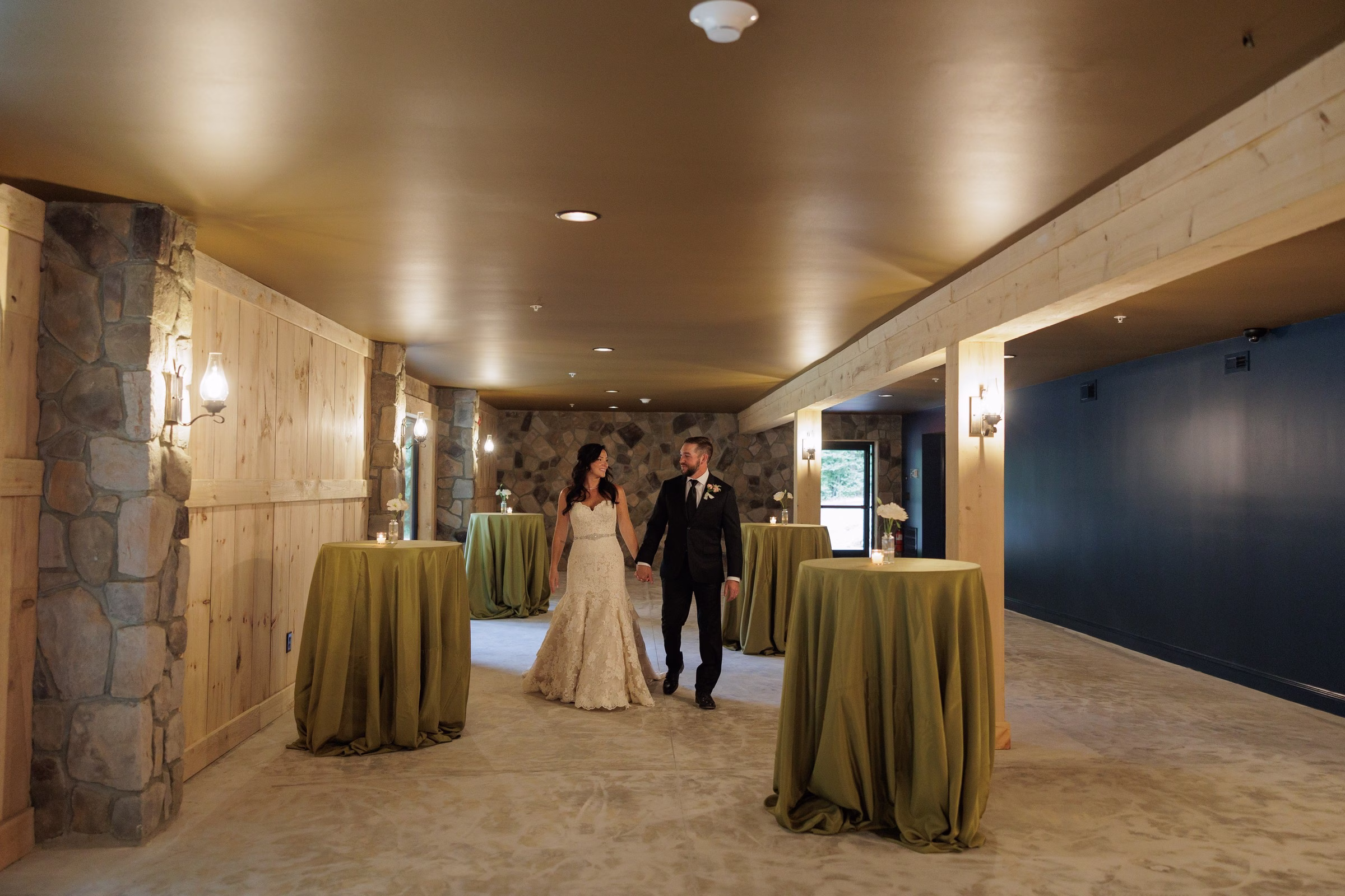 Bride and groom walking hand in hand through the elegant stone and wood cocktail hour hallway at The Grand wedding venue in York SC near Charlotte NC