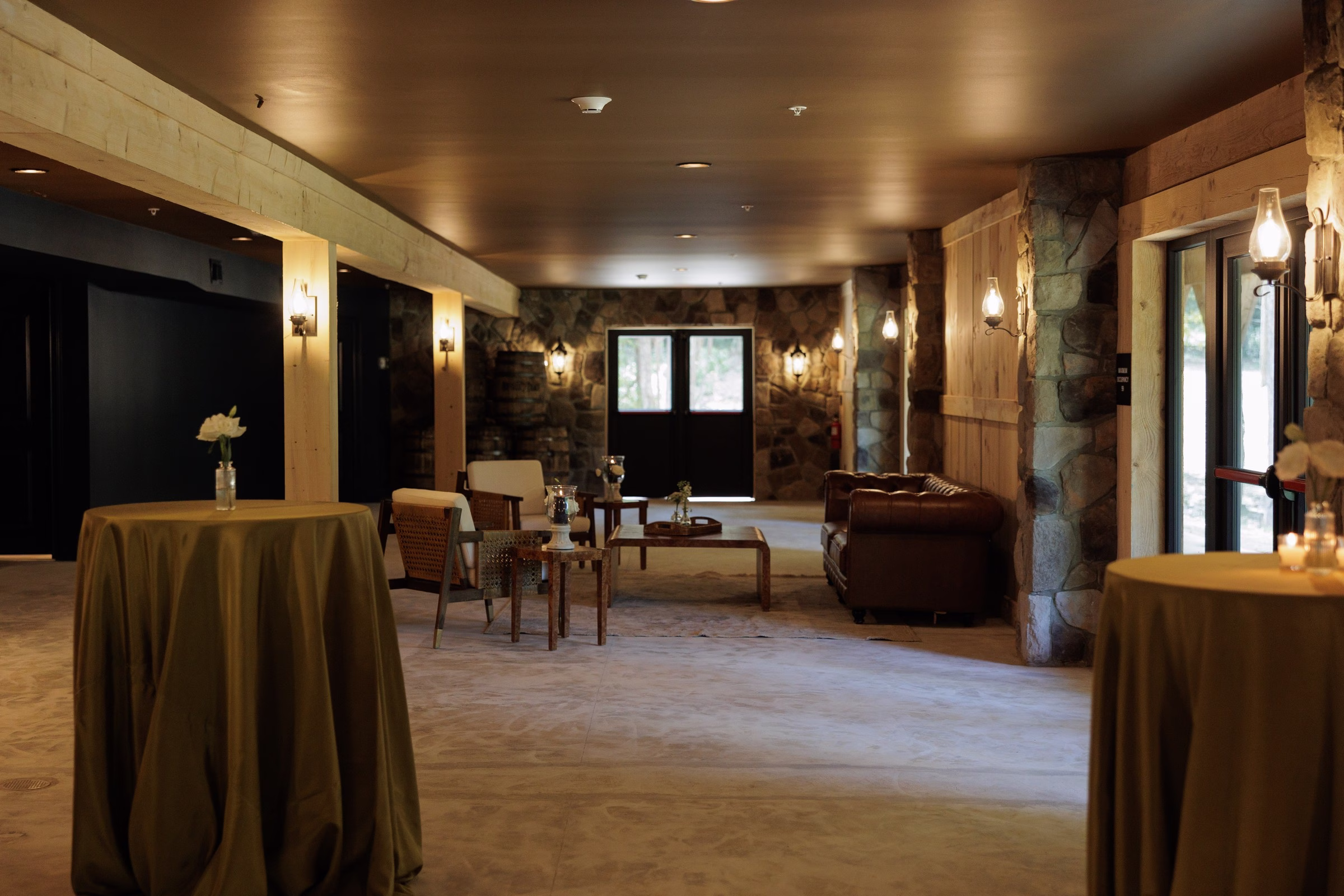 Rustic stone-walled cocktail hour lounge with leather sofas, draped high-top tables, and lantern sconces at The Grand wedding venue in York SC near Charlotte NC
