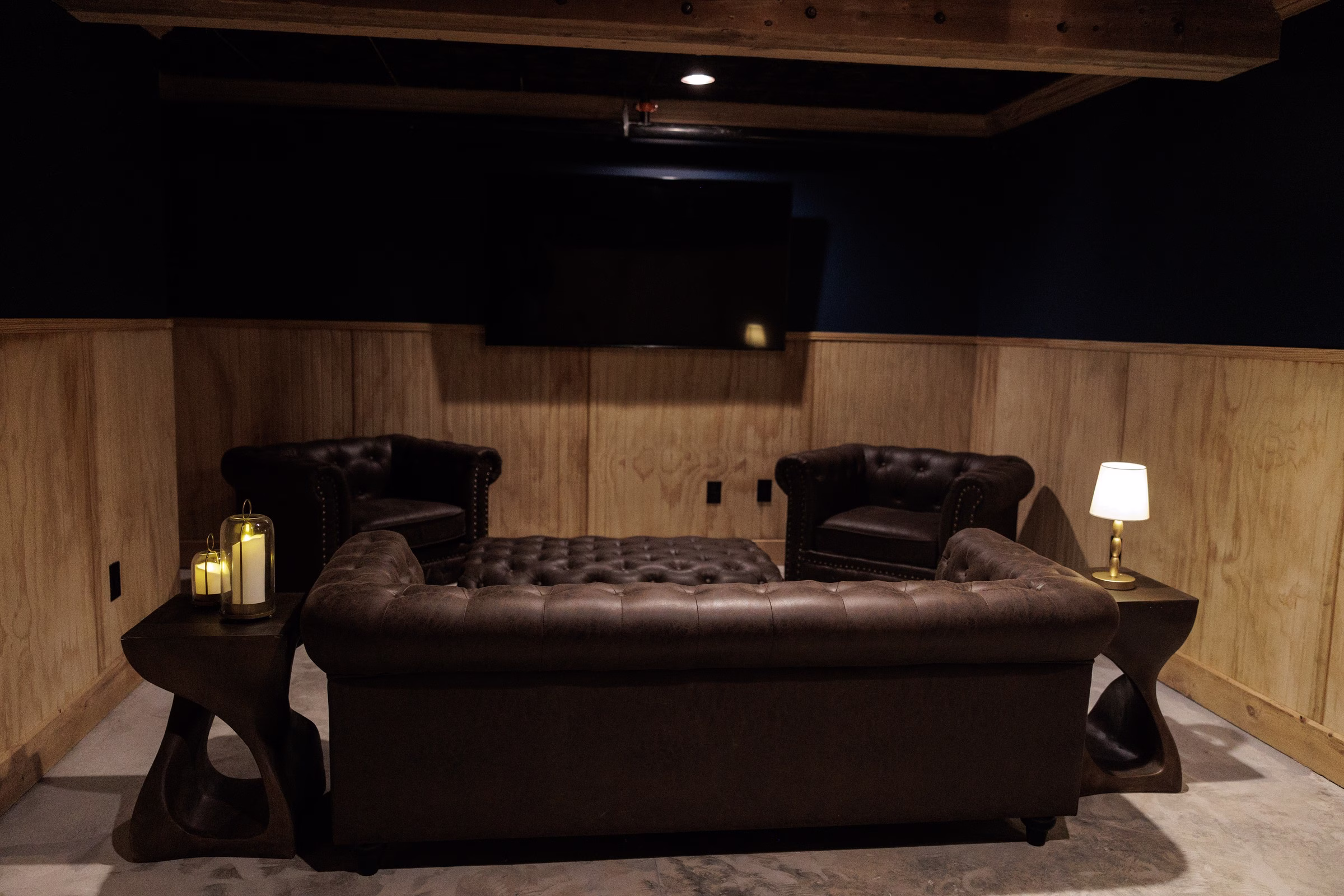 Elegant grooms lounge with dark leather tufted Chesterfield sofa and armchairs, warm candlelight and wood paneling at The Grand wedding venue in York SC near Charlotte NC