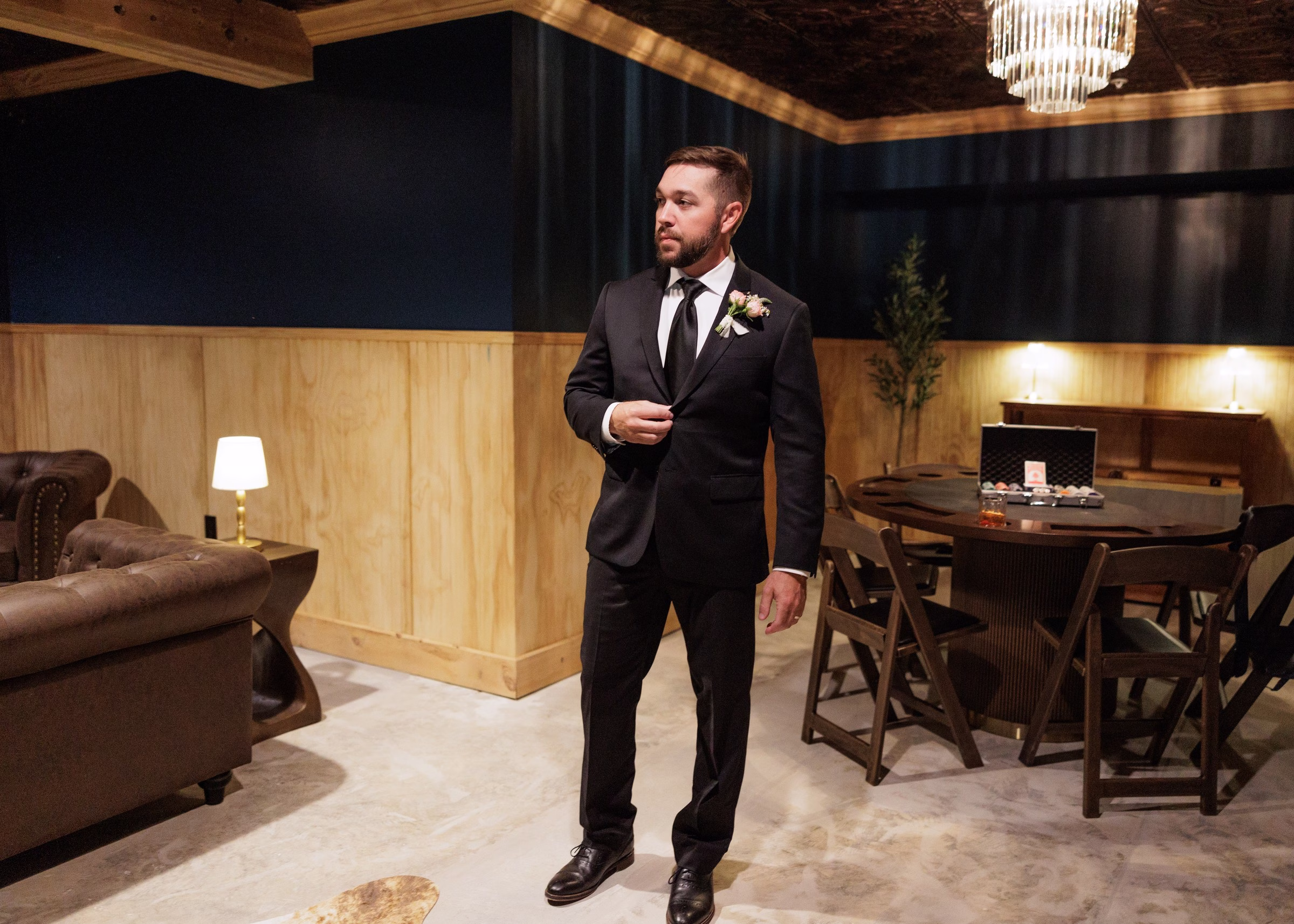 Groom in a dark suit and boutonniere adjusting his jacket in the stylish grooms lounge at The Grand wedding venue in York SC near Charlotte NC
