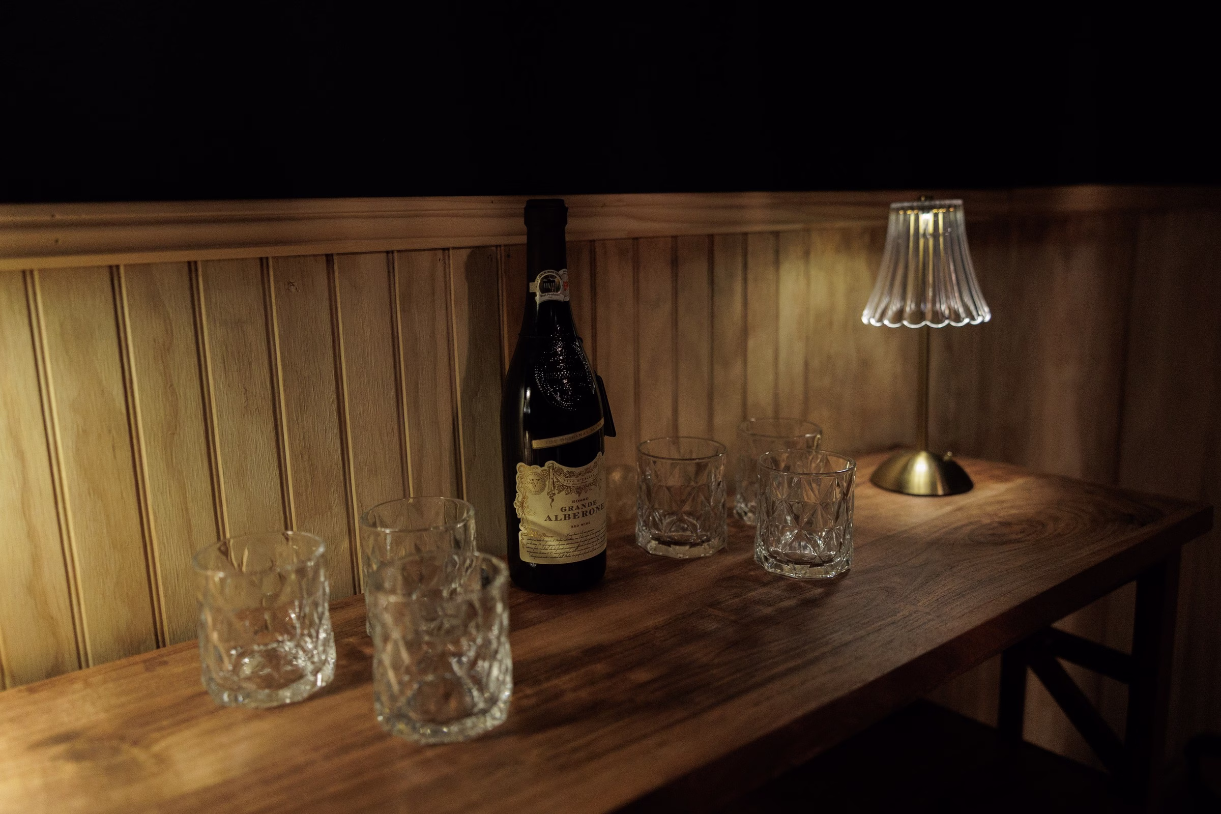 Crystal whiskey glasses and a bottle of Grande Alberone arranged on a dark wood bar in the groom's lounge at The Grand wedding venue in York SC near Charlotte NC