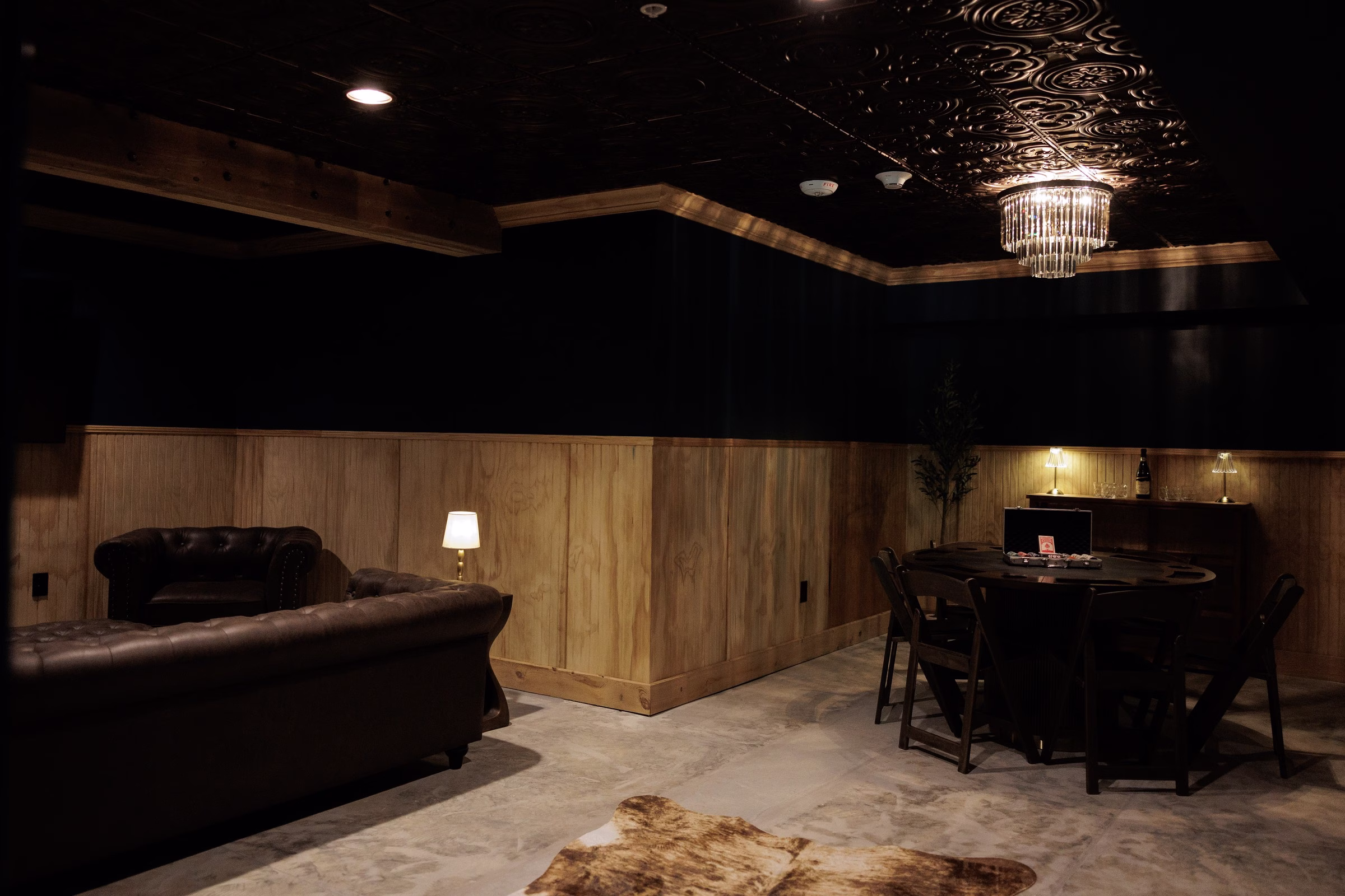 Dark moody speakeasy-style lounge with leather chesterfield sofas, poker table, crystal chandelier, and wood paneling at The Grand wedding venue in York SC near Charlotte NC