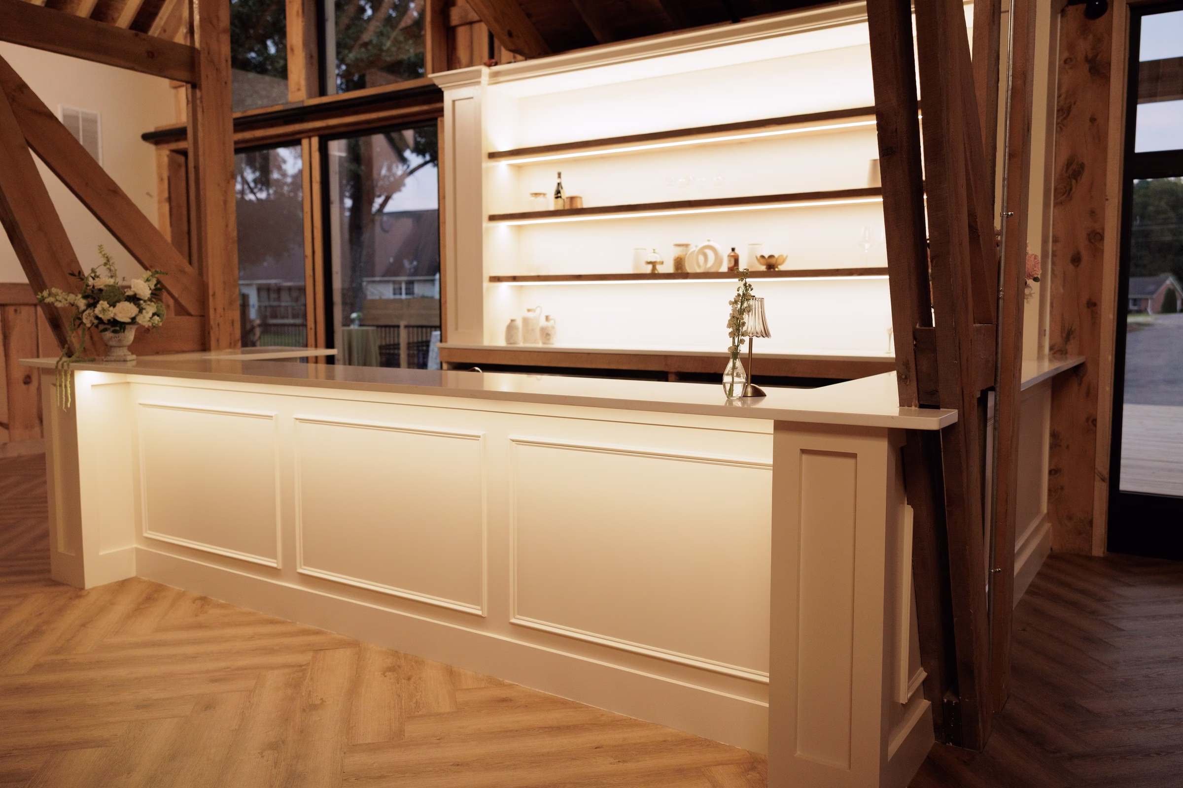 Elegantly lit white paneled bar with floating backlit shelves inside the rustic timber frame wedding venue The Grand in York SC near Charlotte NC