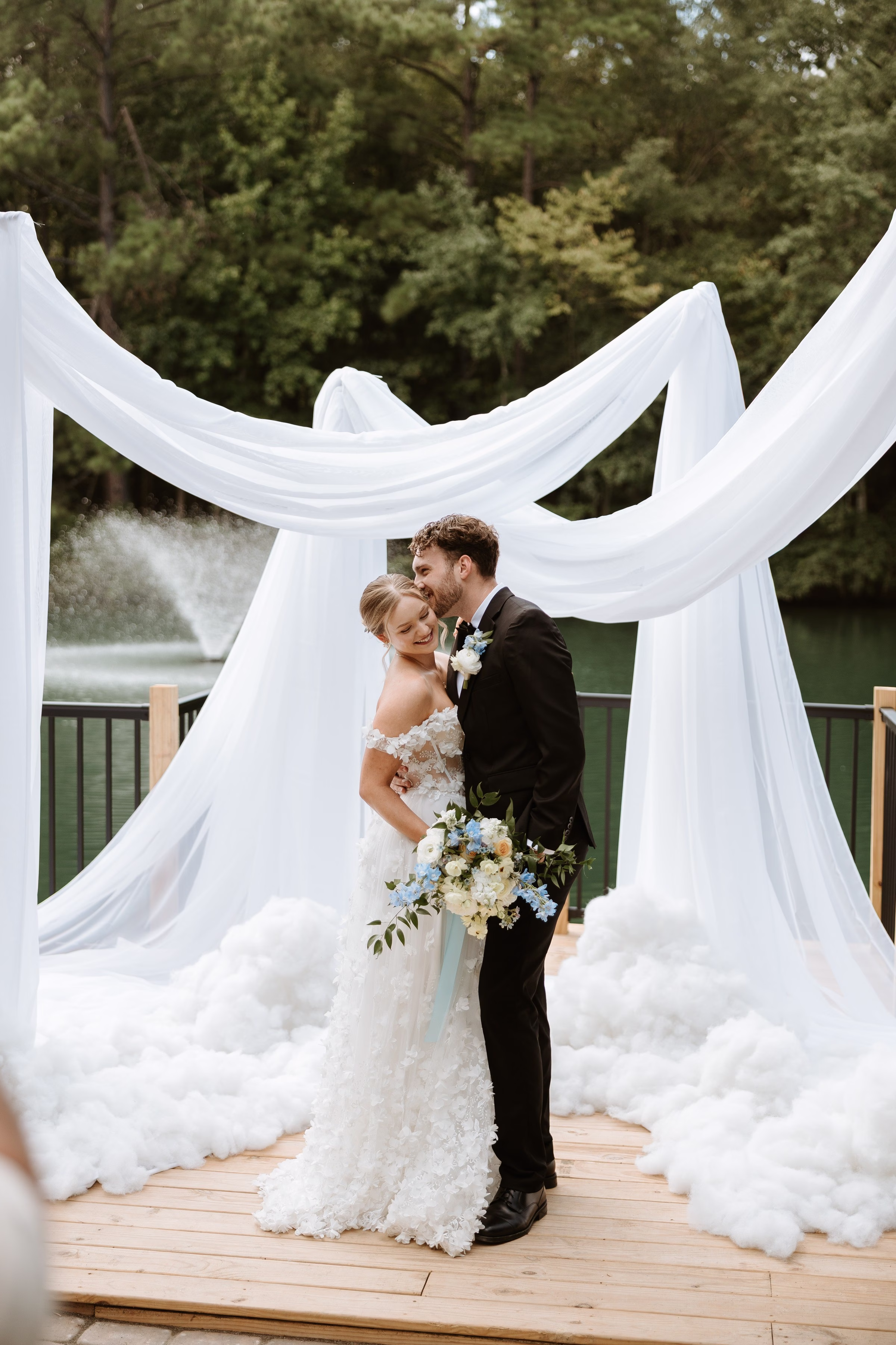 Bride and groom share a romantic moment under white draped altar surrounded by cloud-like decor at The Grand wedding venue in York SC near Charlotte NC