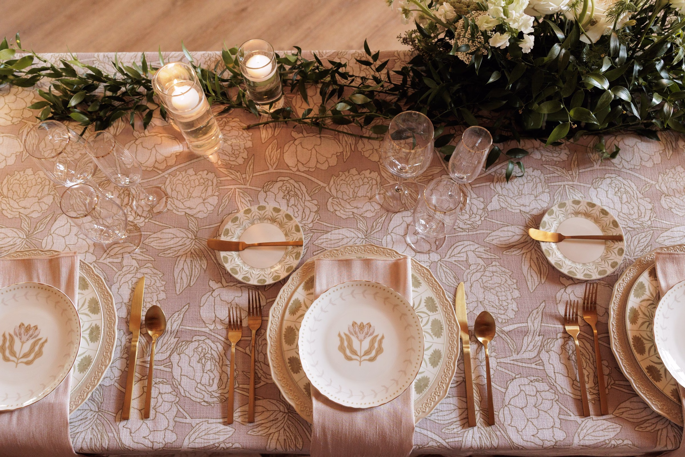 Elegant wedding reception tablescape with gold flatware, floral patterned china, candles, and lush greenery centerpiece at The Grand wedding venue in York SC near Charlotte NC