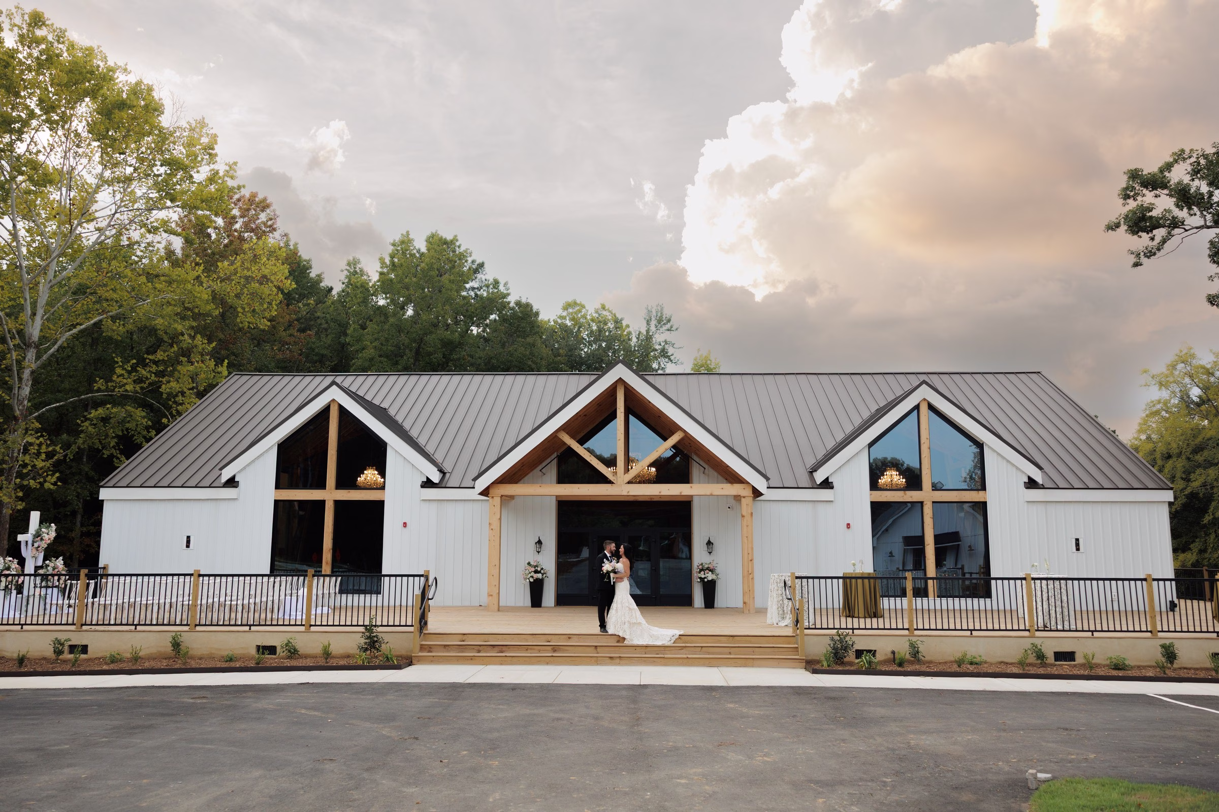 Bride and groom portrait at the entrance of The Grand wedding venue in York SC near Charlotte NC featuring modern farmhouse architecture with white board and batten siding wood beam accents and metal roof at sunset